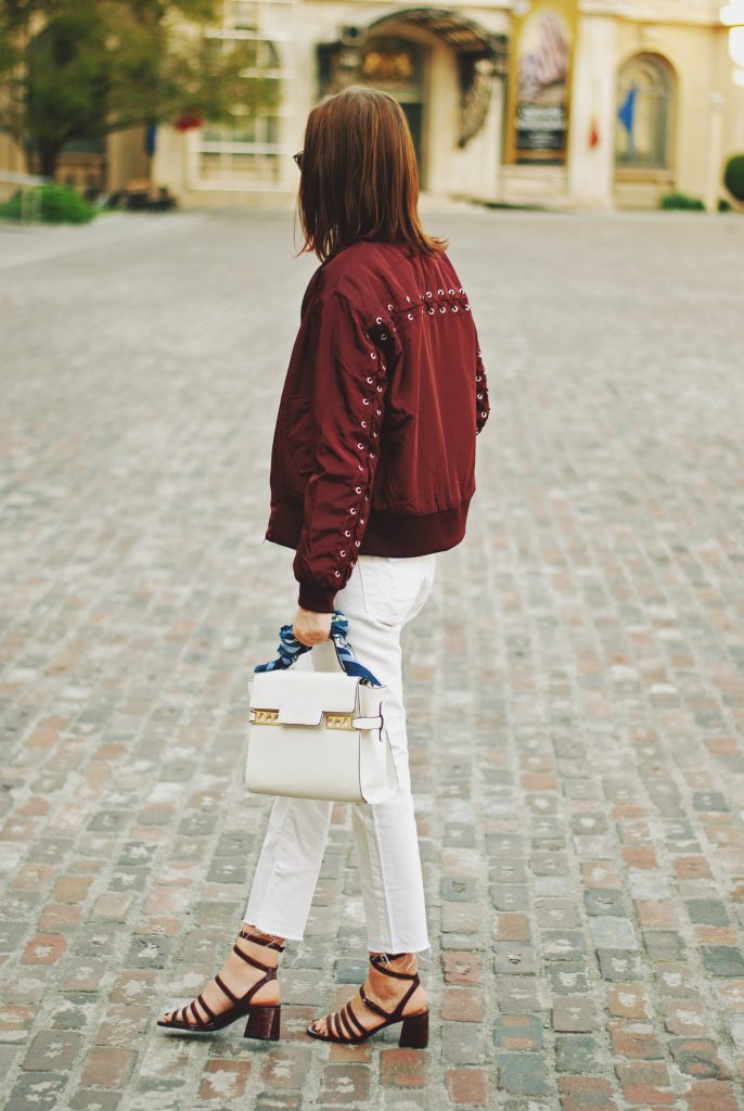 Lace up burgundy bomber jacket, white jeans, strappy sandals, white crossbody bag, sunglasses, fall outfit idea, Andreea Birsan