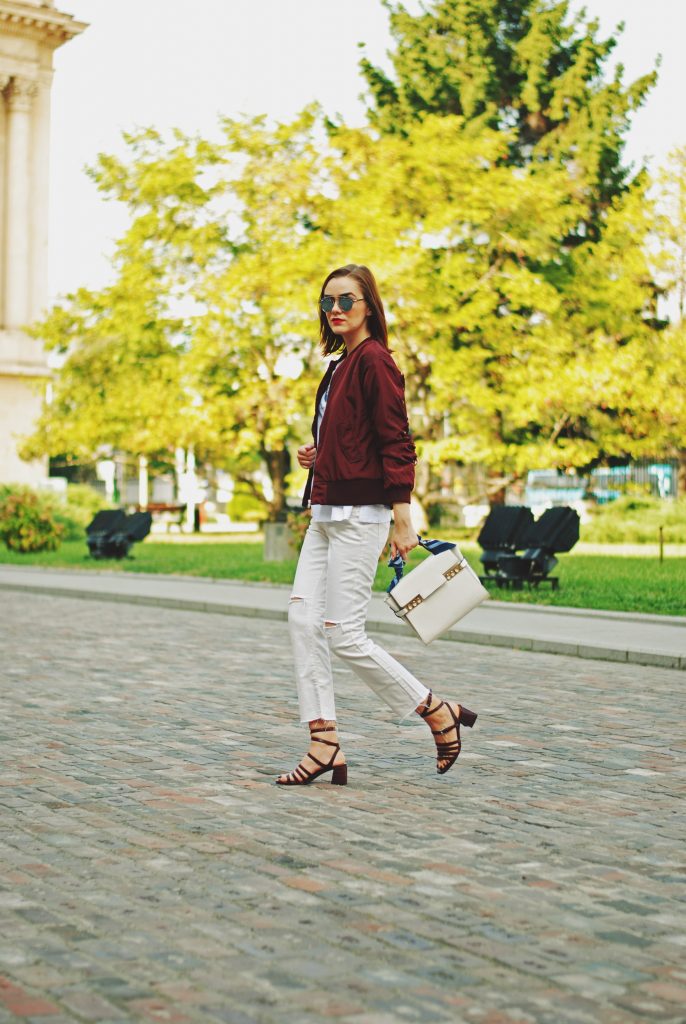 Lace up burgundy bomber jacket, white jeans, strappy sandals, white crossbody bag, sunglasses, fall outfit idea, Andreea Birsan