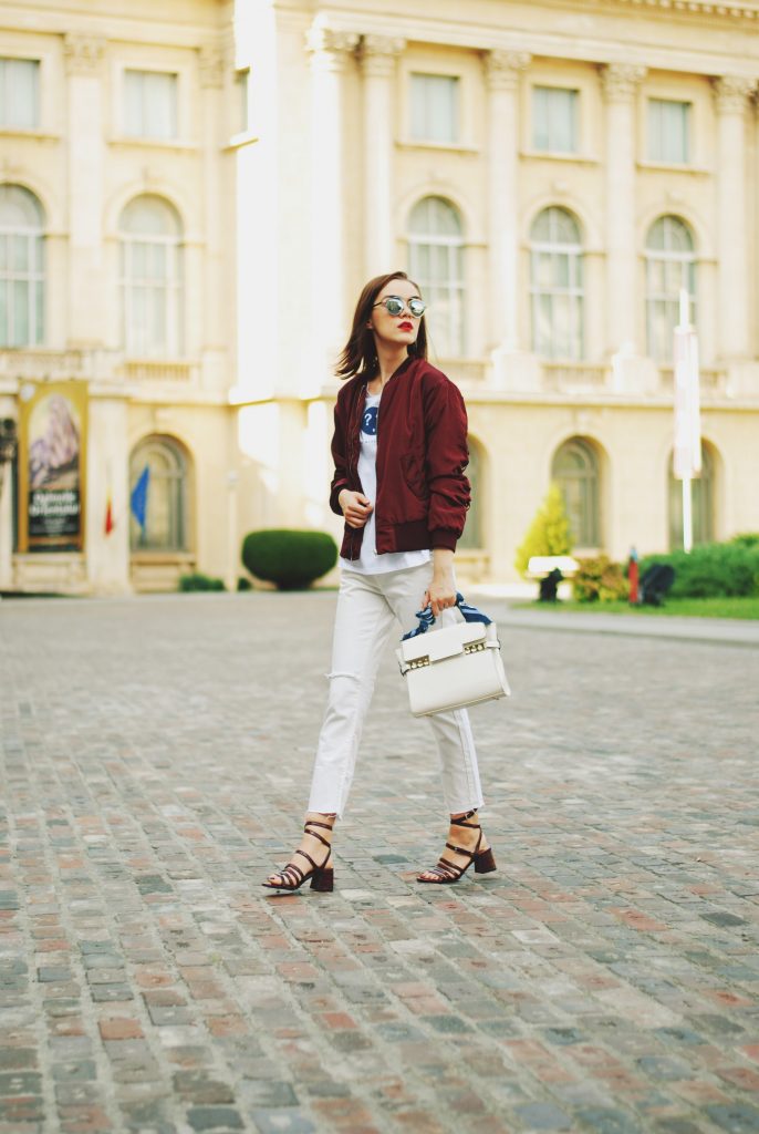 Lace up burgundy bomber jacket, white jeans, strappy sandals, white crossbody bag, sunglasses, fall outfit idea, Andreea Birsan