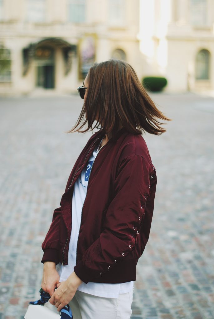 Lace up burgundy bomber jacket, white jeans, strappy sandals, white crossbody bag, sunglasses, fall outfit idea, Andreea Birsan