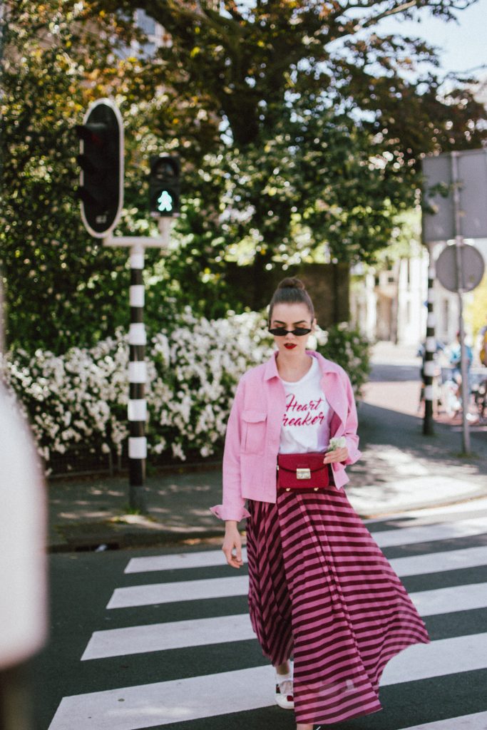 Striped mesh pink and purple skirt, pink cropped cotton jacket, gucci ace sneakers, tshirt, andreea birsan, couturezilla, cute summer outfit for 2018, the color combo you should try this summer pink and purple, pink and purple outfit, ankle length stripe pink mesh skirt, maxi mesh effect skirt, pink striped skirt, long skirt, how to wear a maxi skirt, how to wear a long skirt, what shoes to wear with a maxi skirt, gucci ace heart embroidered white sneakers, gucci white trainers, gucci sneakers with hearts, heart breaker white t-shirt, printed t-shirt, white tee, basic tee, basics, graphic t-shirt, cropped pink cotton jacket, cropped pink denim jacket, denim lookalike jacket, micro sunglasses trend, matrix sunglasses, mini sunglasses, small cat eye sunglasses, fanny bag, belt bag, furla metropolis red bag worn as a belt bag, bum bag, red leather bag, red crossbody bag, genuine leather, pink and purple, how to mix pink and purple, blush pink, mesh effect skirt, skirt and t-shirt, andreea birsan in the netherlands, holland, travel diary, den haag, couturezilla travels, travel outfit, traveling girl look, holland, how to look Parisian chic, European summer street style inspiration for women 2017, pinterest chic outfit ideas for woman, summer outfit ideas, summer ootd inspiration, outfit of the day, ootd, fashion icon, style inspiration, fashionista, fashion inspiration, style inspo, what to wear in summer, how to look French, chic on a budget, zara outfit, mango, topshop, asos, river island, forever 21, urban outfitters, how to mix high end pieces with luxury ones, zara and Gucci,outfit alternatives for summer, tomboy chic, minimal outfit, tumblr girls photos, pictures, happy girl, women, smart casual outfits, the best outfit ideas 2017, what to wear when you don’t feel inspired, summer in Europe, weekend attire, uniform, French women in summer, European outfit ideas 2017, minimal chic outfit, how to stand out, the best outfit ideas for summer, the sunglasses you have seen everywhere on Instagram, glasses, uk fashion blogger, united kingdom, uk fashion blog, fashion and travel blog, Europe, women with style, street style, summer fashion trends 2017, best fashion ideas, styling, fall fashion, fall outfit, fall ootd, fall perfect, transitional dressing, best transitional outfit ideas, how to wear statement earrings, dressing for autumn, autumn outfit, winter outfit ideas for work and school 2017