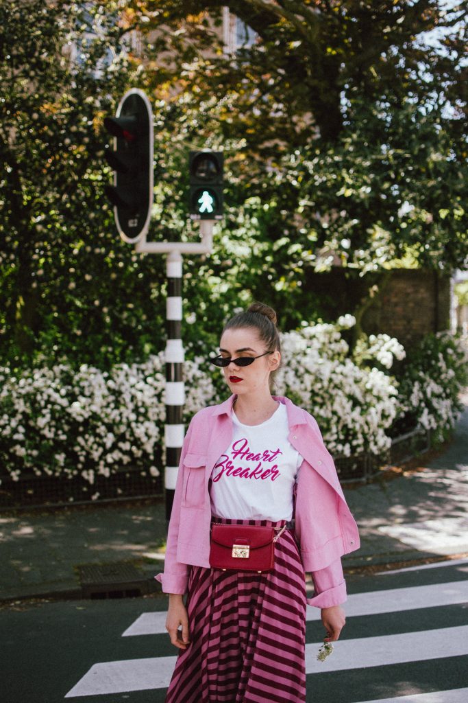 Striped mesh pink and purple skirt, pink cropped cotton jacket, gucci ace sneakers, tshirt, andreea birsan, couturezilla, cute summer outfit for 2018, the color combo you should try this summer pink and purple, pink and purple outfit, ankle length stripe pink mesh skirt, maxi mesh effect skirt, pink striped skirt, long skirt, how to wear a maxi skirt, how to wear a long skirt, what shoes to wear with a maxi skirt, gucci ace heart embroidered white sneakers, gucci white trainers, gucci sneakers with hearts, heart breaker white t-shirt, printed t-shirt, white tee, basic tee, basics, graphic t-shirt, cropped pink cotton jacket, cropped pink denim jacket, denim lookalike jacket, micro sunglasses trend, matrix sunglasses, mini sunglasses, small cat eye sunglasses, fanny bag, belt bag, furla metropolis red bag worn as a belt bag, bum bag, red leather bag, red crossbody bag, genuine leather, pink and purple, how to mix pink and purple, blush pink, mesh effect skirt, skirt and t-shirt, andreea birsan in the netherlands, holland, travel diary, den haag, couturezilla travels, travel outfit, traveling girl look, holland, how to look Parisian chic, European summer street style inspiration for women 2017, pinterest chic outfit ideas for woman, summer outfit ideas, summer ootd inspiration, outfit of the day, ootd, fashion icon, style inspiration, fashionista, fashion inspiration, style inspo, what to wear in summer, how to look French, chic on a budget, zara outfit, mango, topshop, asos, river island, forever 21, urban outfitters, how to mix high end pieces with luxury ones, zara and Gucci,outfit alternatives for summer, tomboy chic, minimal outfit, tumblr girls photos, pictures, happy girl, women, smart casual outfits, the best outfit ideas 2017, what to wear when you don’t feel inspired, summer in Europe, weekend attire, uniform, French women in summer, European outfit ideas 2017, minimal chic outfit, how to stand out, the best outfit ideas for summer, the sunglasses you have seen everywhere on Instagram, glasses, uk fashion blogger, united kingdom, uk fashion blog, fashion and travel blog, Europe, women with style, street style, summer fashion trends 2017, best fashion ideas, styling, fall fashion, fall outfit, fall ootd, fall perfect, transitional dressing, best transitional outfit ideas, how to wear statement earrings, dressing for autumn, autumn outfit, winter outfit ideas for work and school 2017